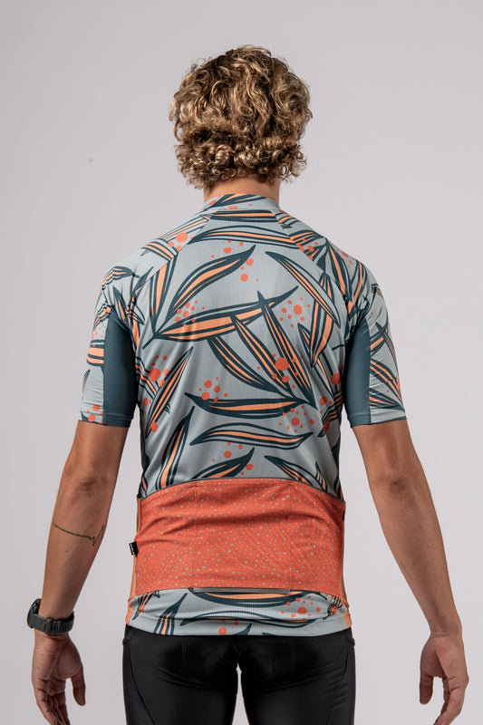 Back of model pose to showcase the pockets on the Varlo pioneer gravel series cycling jersey in floral pattern and mora orange color.