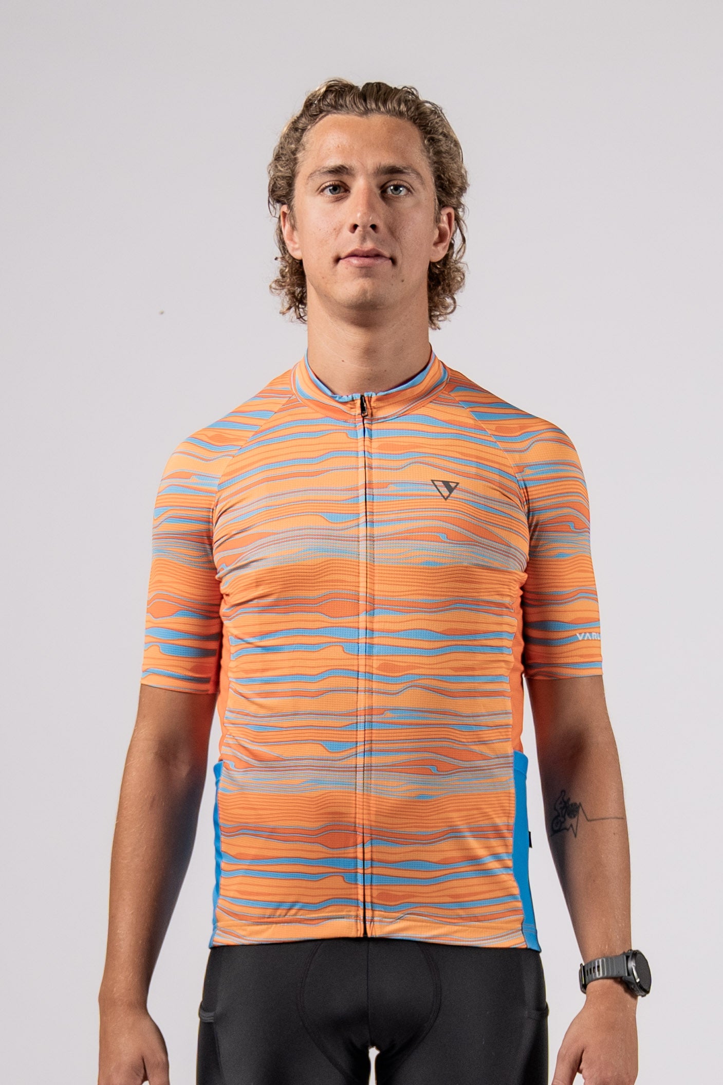Front view in studio of male model of the pioneer gravel jersey in path orange from the Varlo 2025 gravel series.